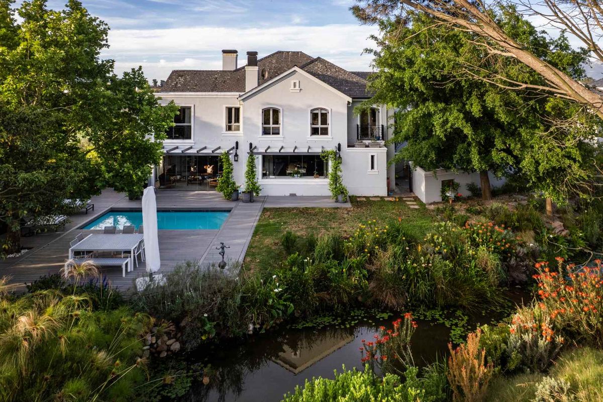 Rear view of a two-story residence featuring a swimming pool, timber decking, and a landscaped garden with a pond.