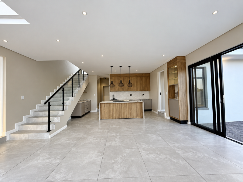 Spacious open-plan living area featuring a modern kitchen with island, sleek cabinetry, tiled floors, and a contemporary staircase with glass balustrade.