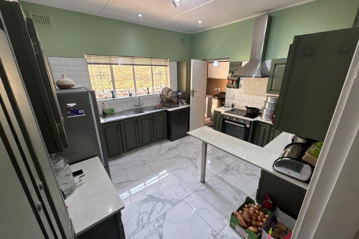 A well-lit kitchen featuring olive green cabinetry, white subway tile backsplash, stone-look countertops, marble-effect floor tiles, and a stainless steel extractor fan.