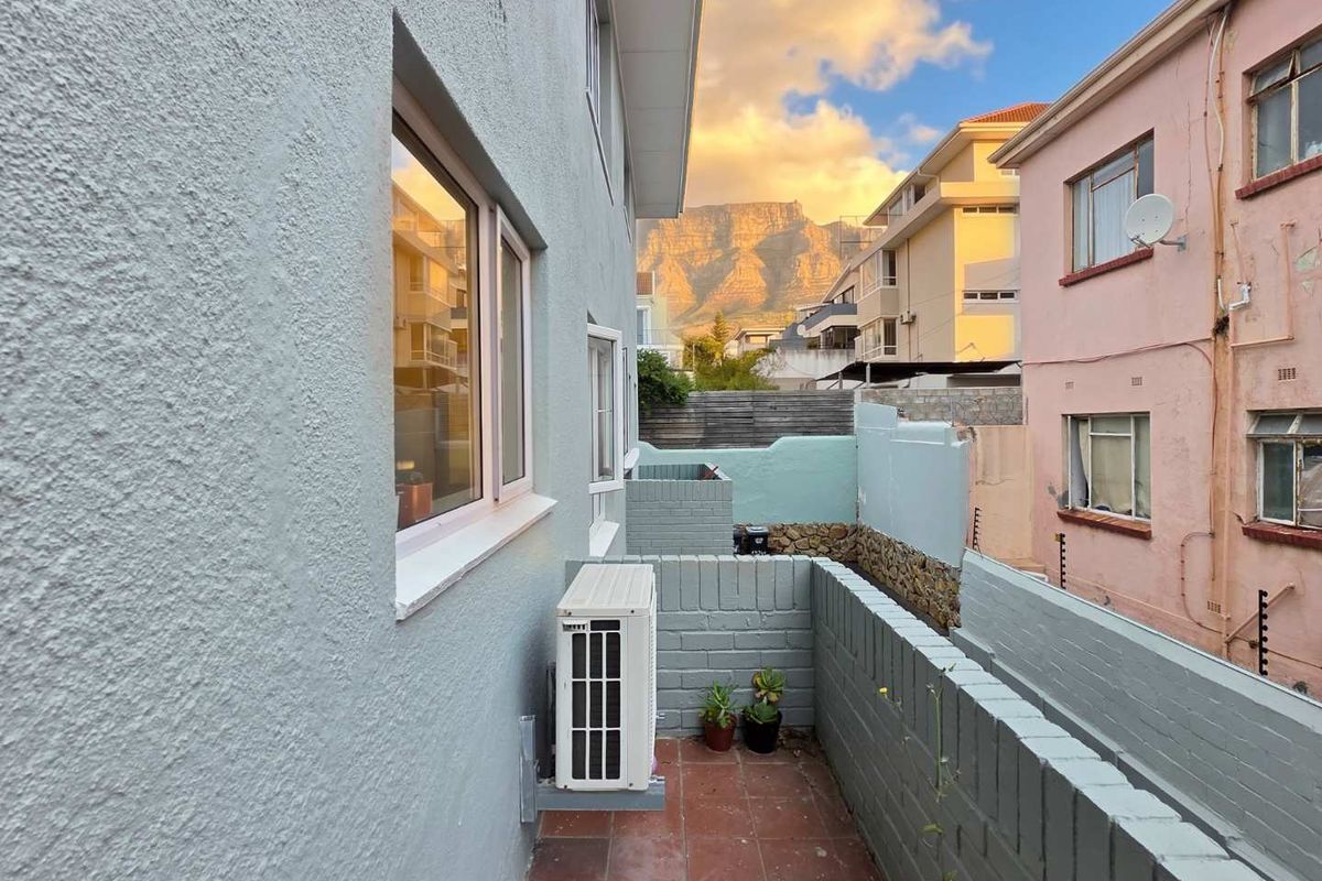 Rear exterior view of the apartment featuring a tiled patio area, brick boundary walls, and a scenic mountain view at sunset.
