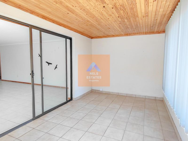 An enclosed patio or sunroom featuring tiled flooring, a timber ceiling, and large sliding glass doors leading to the main living area.