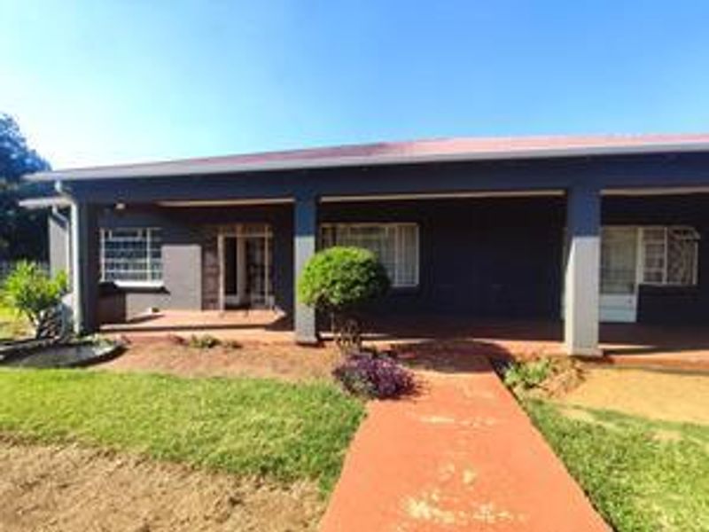 A rear view of the house featuring a covered patio area, concrete columns, and a paved walkway leading to the garden.