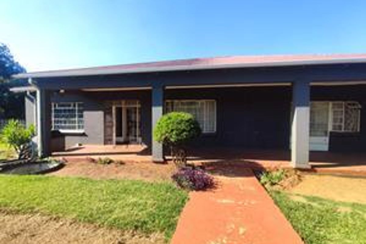 A rear view of the house featuring a covered patio area, concrete columns, and a paved walkway leading to the garden.