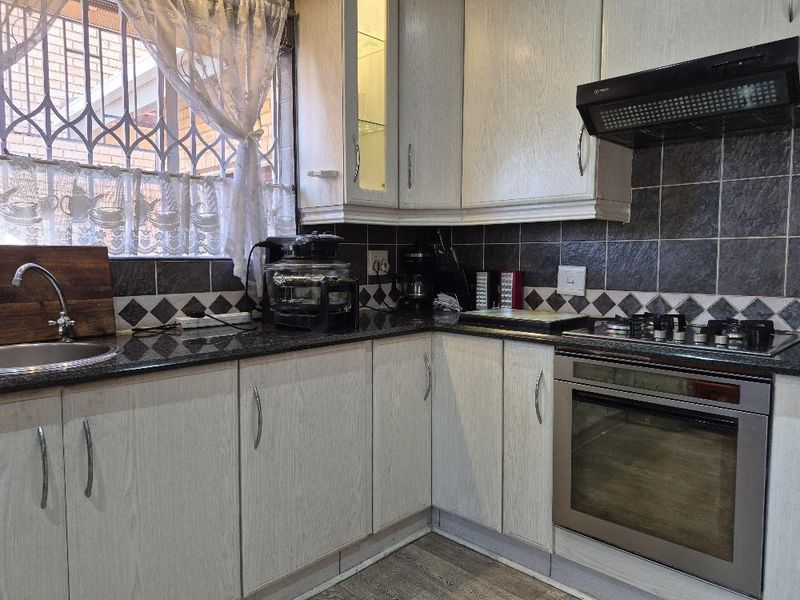 A functional kitchen featuring light wood-grain cabinetry, dark granite countertops, a built-in oven with gas hob, and a tiled backsplash.
