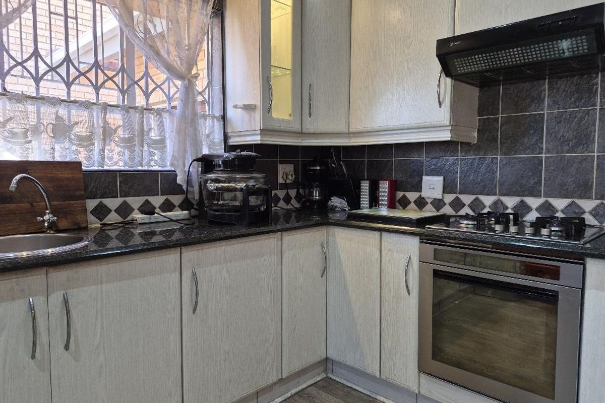 A functional kitchen featuring light wood-grain cabinetry, dark granite countertops, a built-in oven with gas hob, and a tiled backsplash.