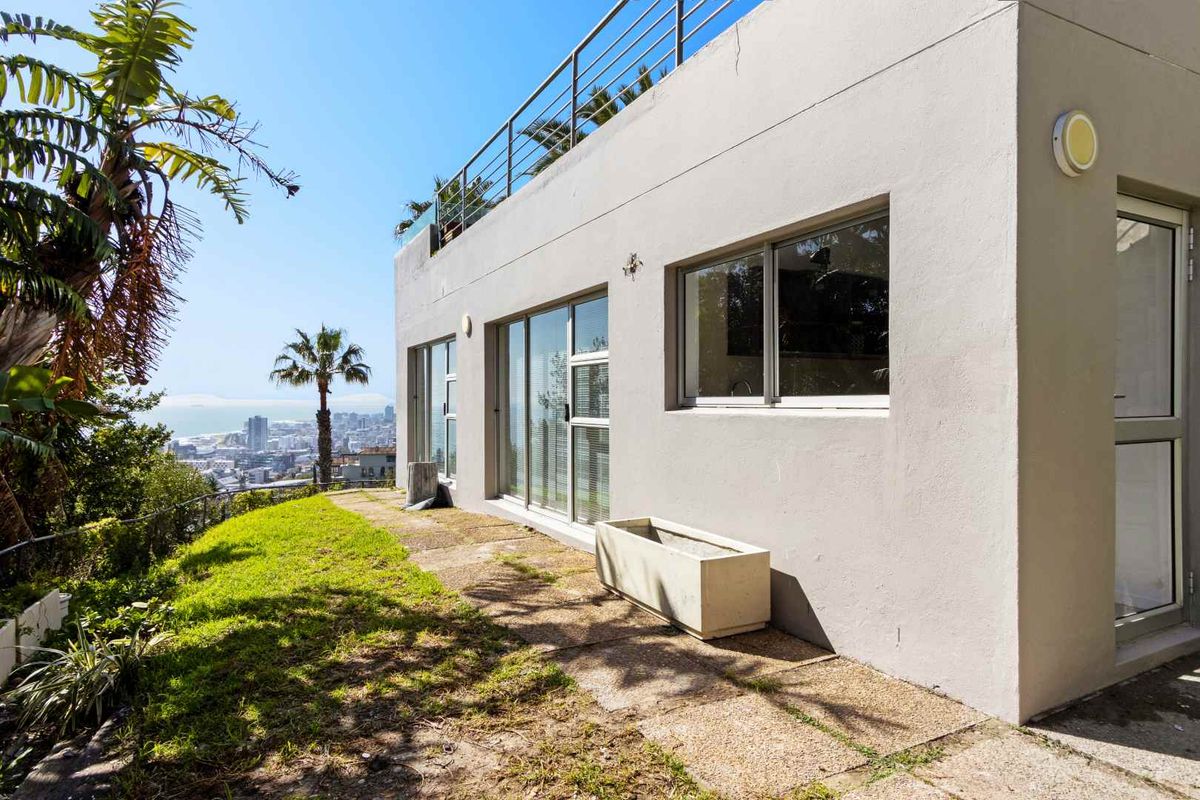 Exterior view of the property featuring a paved patio area, sliding glass doors, and a rooftop balcony with metal railings overlooking the city.