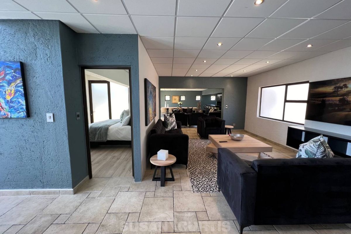 Spacious living area featuring tiled flooring, recessed downlighting, and a drop ceiling, with an adjacent bedroom visible through the doorway.