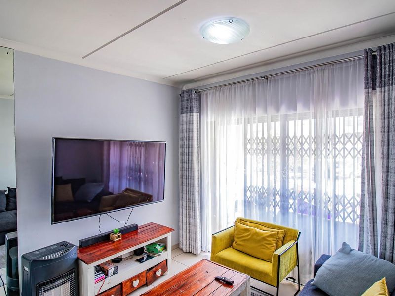 A comfortable living room featuring tiled flooring and a large sliding glass door with security gate, providing access to the exterior.