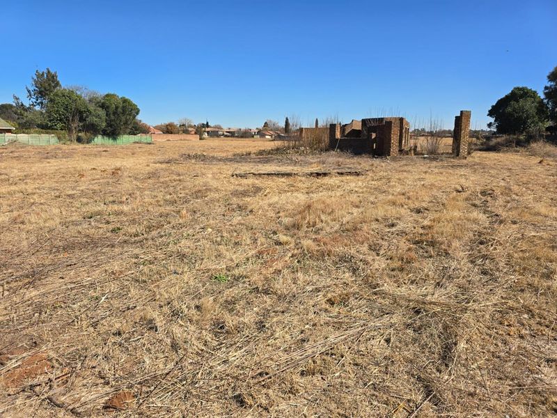 A large vacant residential plot featuring dry grass and the remains of a brick structure, offering potential for new development.
