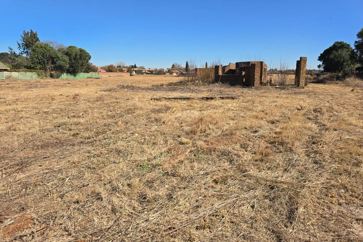A large vacant residential plot featuring dry grass and the remains of a brick structure, offering potential for new development.