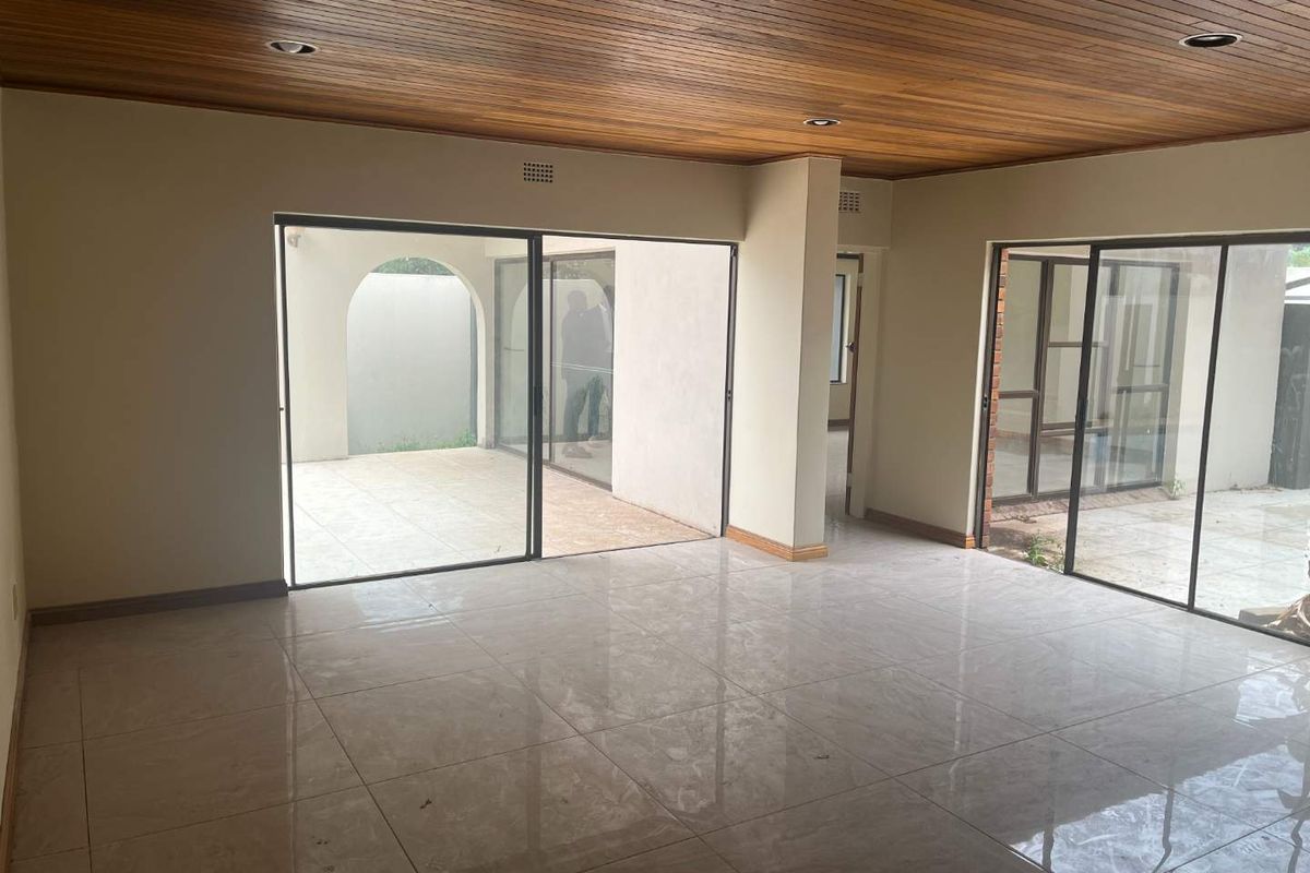 Spacious living area featuring polished floor tiles, a warm timber-paneled ceiling, and large sliding glass doors providing seamless access to the outdoor patio.