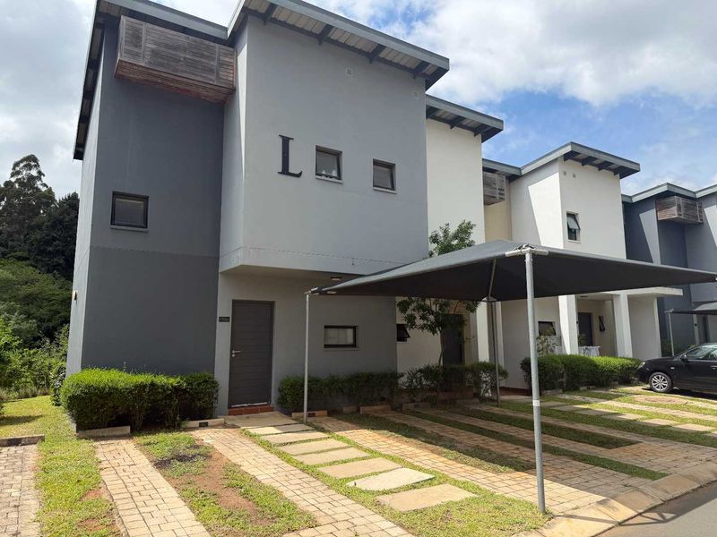 Modern townhouse exterior featuring a paved driveway, shade sail carport, and contemporary grey and white facade with timber accents.
