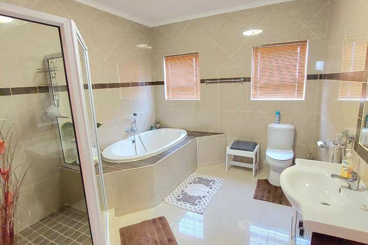 A well-maintained bathroom featuring a built-in bathtub, separate glass shower enclosure, pedestal washbasin, and neutral wall tiling.
