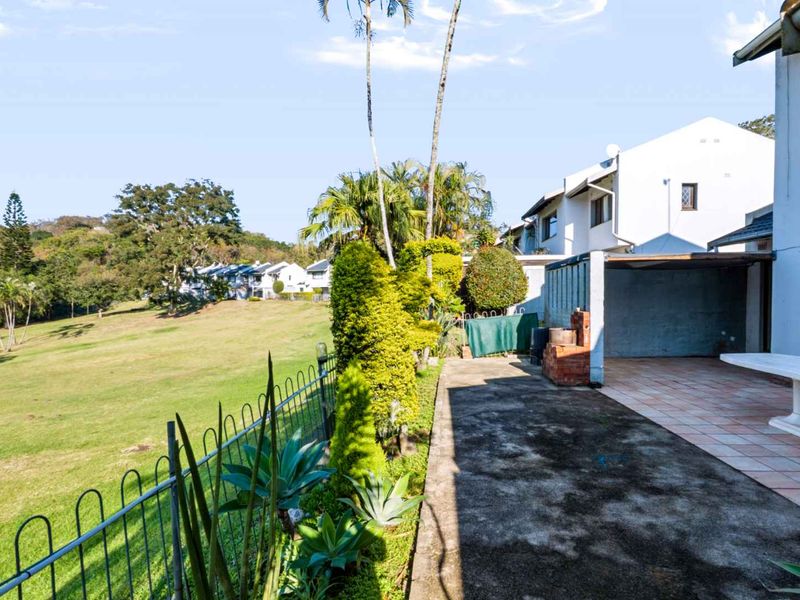 Rear exterior view of the townhouse featuring a tiled patio, built-in brick braai, and direct access to the communal garden area.