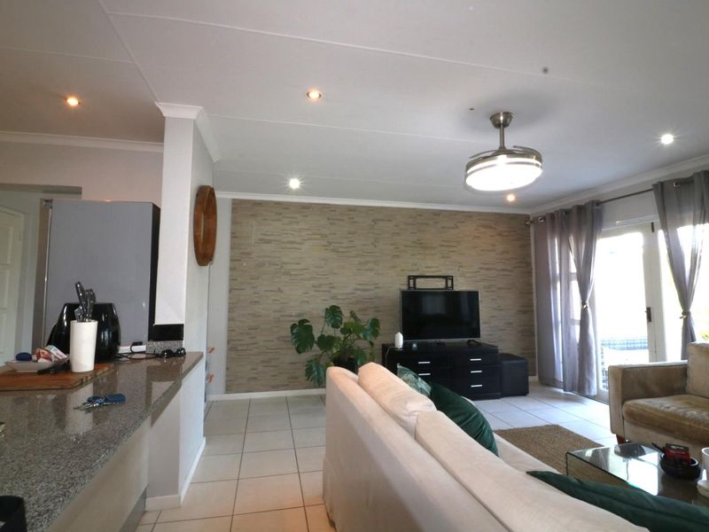 Open-plan living area featuring a granite kitchen counter, stone-cladding feature wall, tiled floors, and direct access to the patio through sliding glass doors.