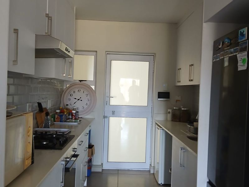 A functional galley-style kitchen featuring white cabinetry, subway tile backsplash, gas hob, under-counter oven, and direct access to an exterior door.