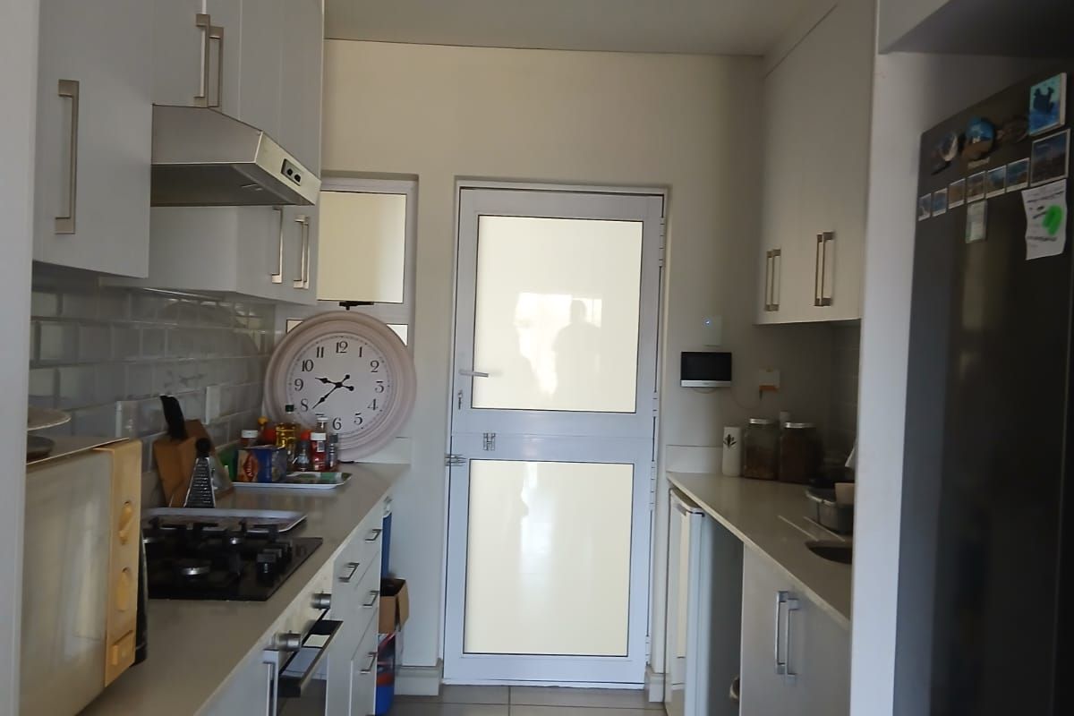 A functional galley-style kitchen featuring white cabinetry, subway tile backsplash, gas hob, under-counter oven, and direct access to an exterior door.