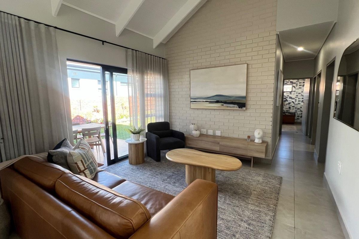 Bright living room featuring a vaulted ceiling with exposed beams, a painted brick feature wall, and sliding glass doors leading to the patio.