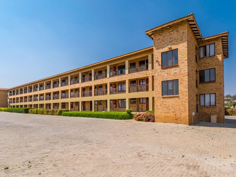 A multi-story apartment complex featuring a face brick facade, tiled roof, and private balconies, set within a well-maintained paved exterior area.