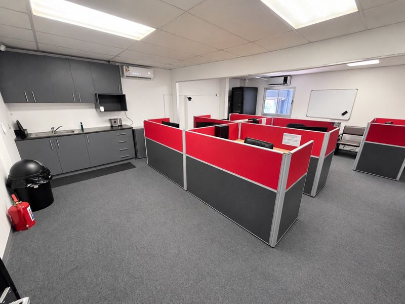 A functional office space featuring modular workstations, a kitchenette with built-in cabinetry, sink, and split-system air conditioning units.