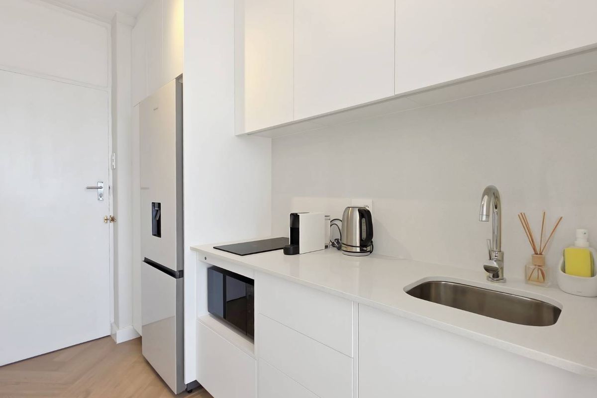 Modern, minimalist kitchen featuring sleek white cabinetry, stone countertops, integrated microwave, induction cooktop, and a stainless steel undermount sink.