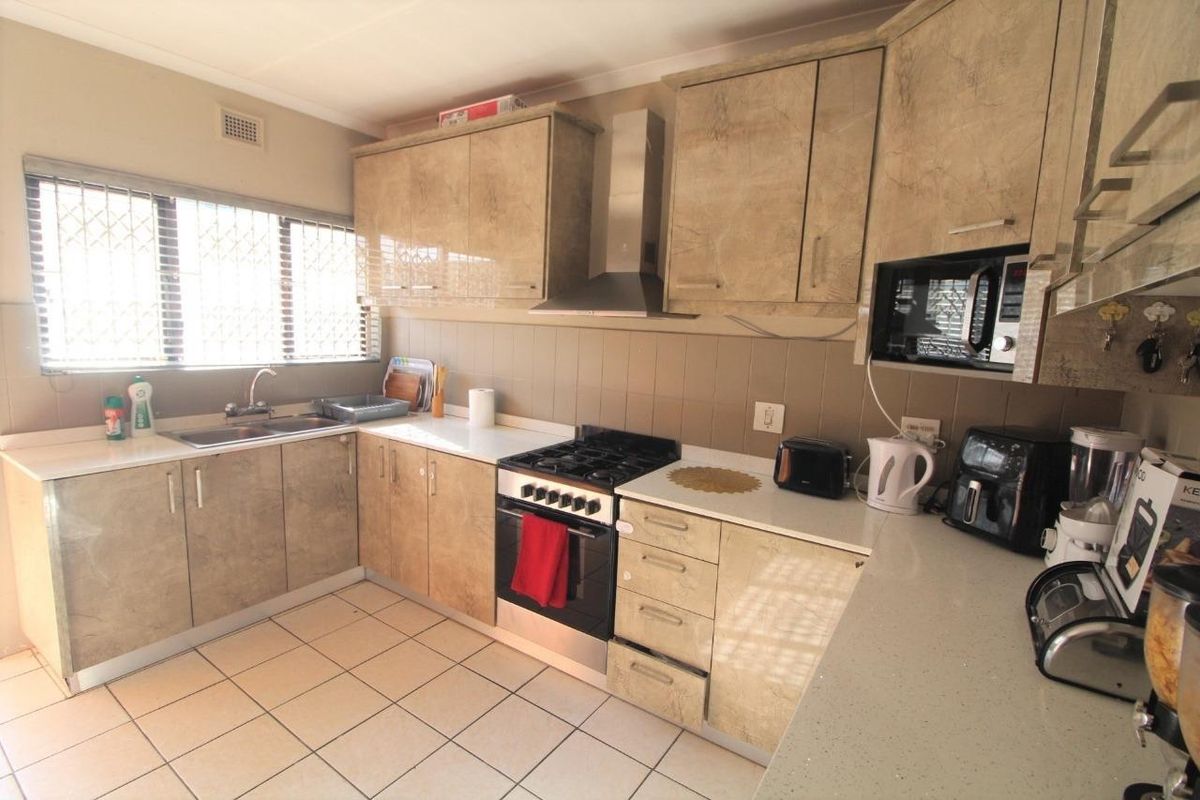 Functional kitchen featuring laminate cabinetry, stainless steel extractor fan, built-in oven, gas hob, and tiled flooring with a double bowl sink.