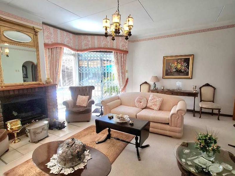 Spacious living room featuring a brick fireplace, classic chandelier lighting, and a large bay window with security gate access to the exterior.