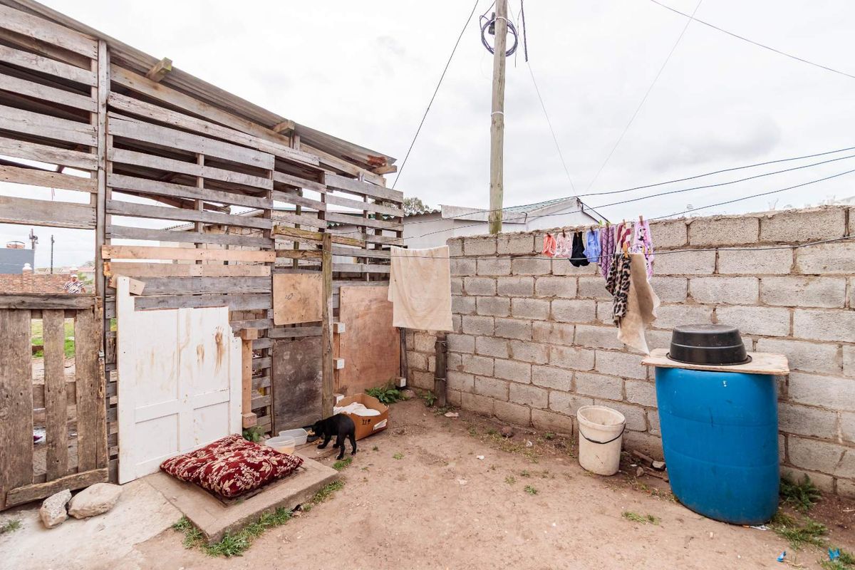 An outdoor utility area featuring a makeshift timber structure and a concrete block boundary wall.