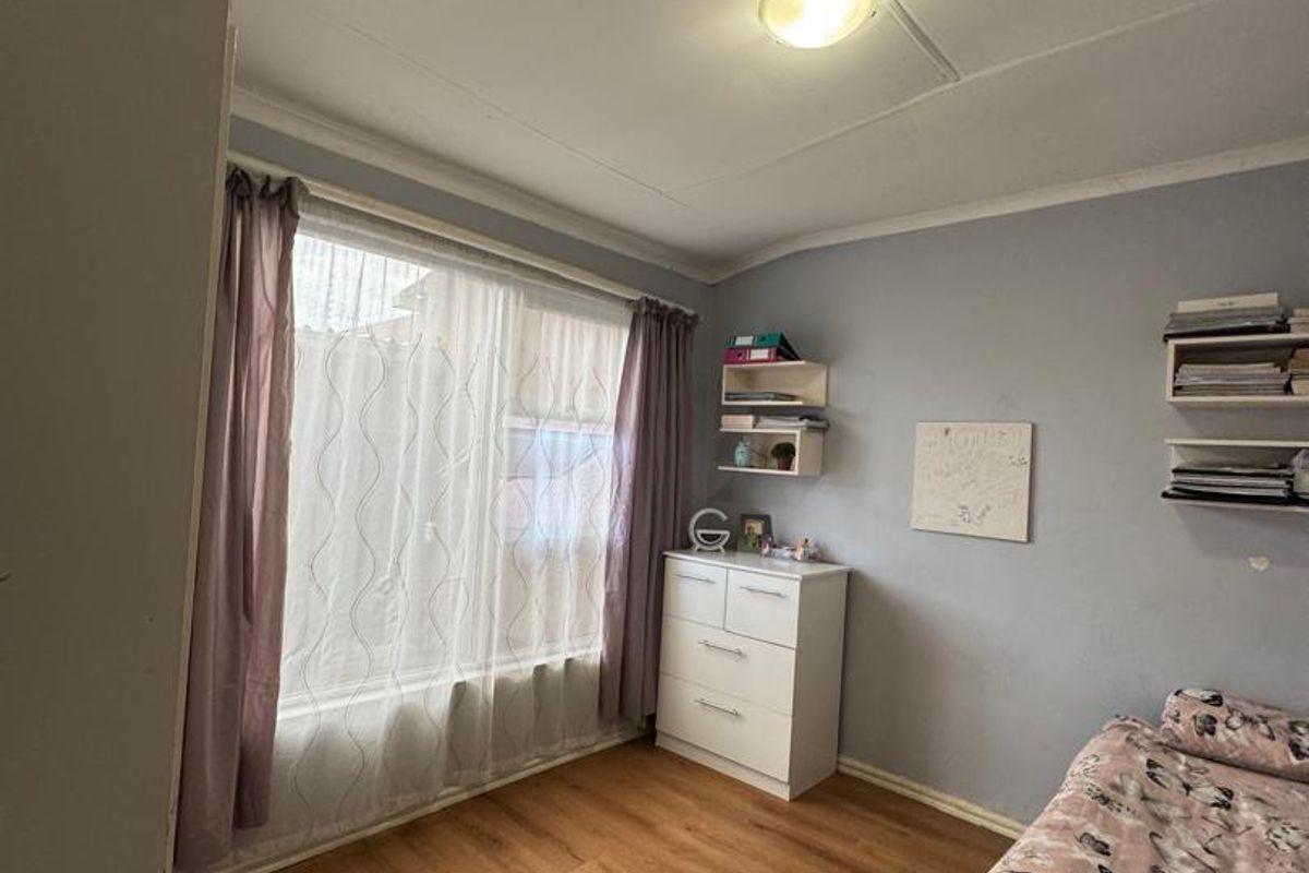 A standard bedroom featuring laminate flooring, a large window with curtains, and wall-mounted shelving units.