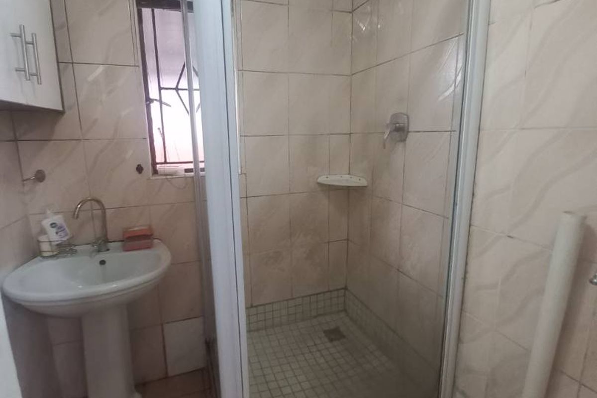 A compact bathroom featuring a pedestal basin, a tiled shower enclosure with a glass door, and ceramic wall and floor tiling.