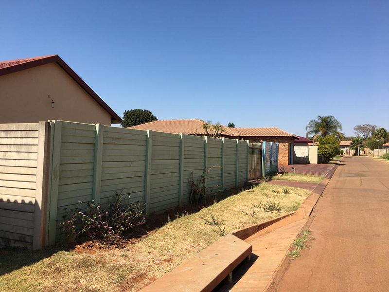 A street-level view of the property showing the precast concrete boundary wall, tiled roof structure, and paved driveway access.