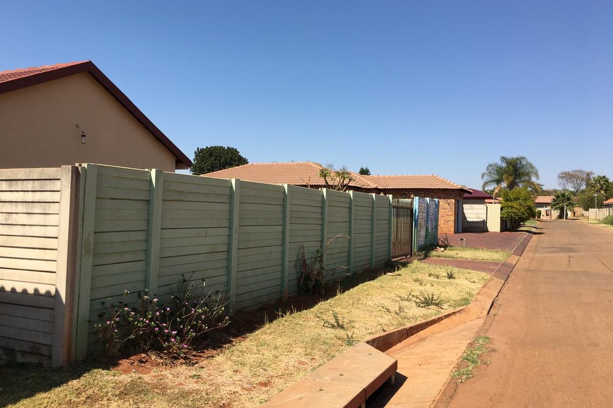A street-level view of the property showing the precast concrete boundary wall, tiled roof structure, and paved driveway access.