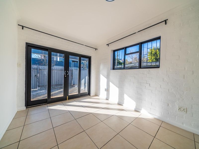 Bright and airy living space featuring white painted brick walls, neutral tiled flooring, and large sliding glass doors providing access to the exterior.