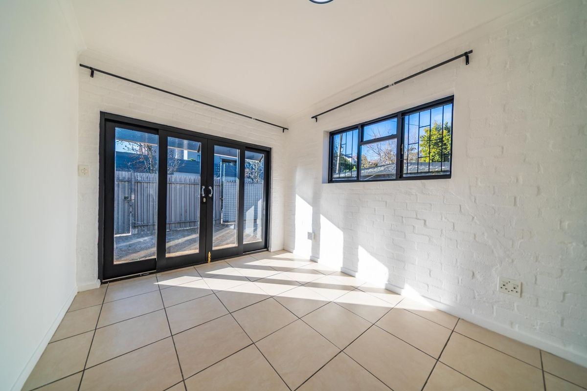 Bright and airy living space featuring white painted brick walls, neutral tiled flooring, and large sliding glass doors providing access to the exterior.