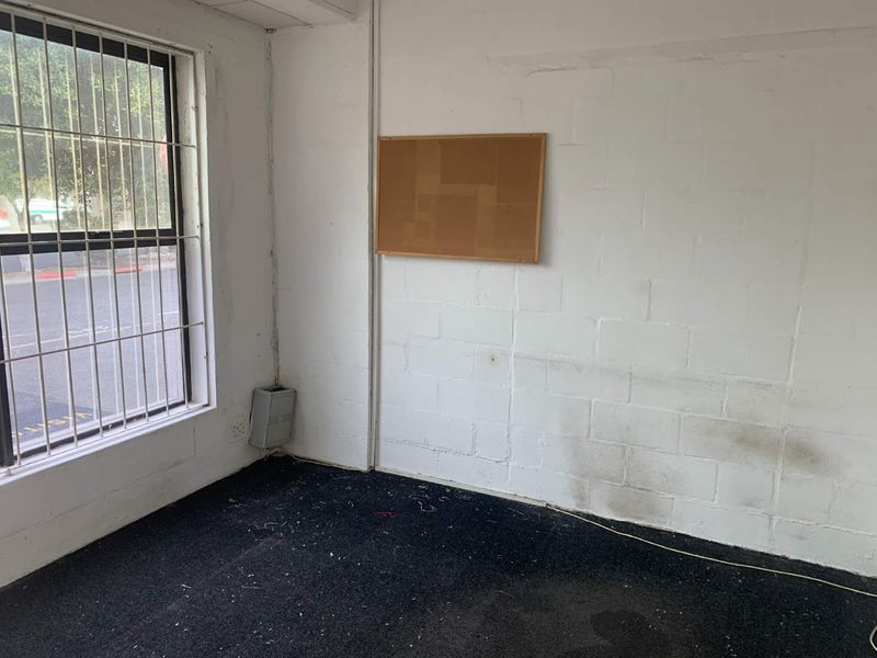 An empty office space featuring exposed brick walls, security bars on the window, and dark carpeting in need of refurbishment.