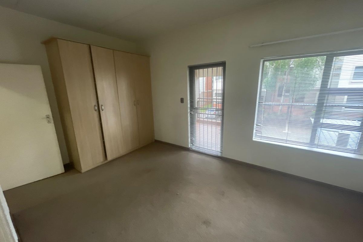 An empty bedroom featuring built-in cupboards, carpeted flooring, and a security gate leading to an outdoor area.