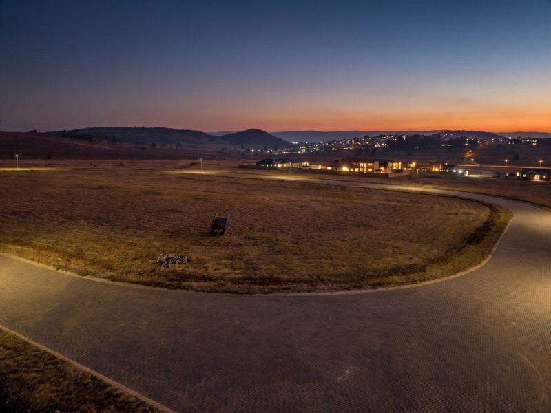 Aerial view of a vacant residential plot at dusk, featuring paved road access and established street lighting in a developing estate.