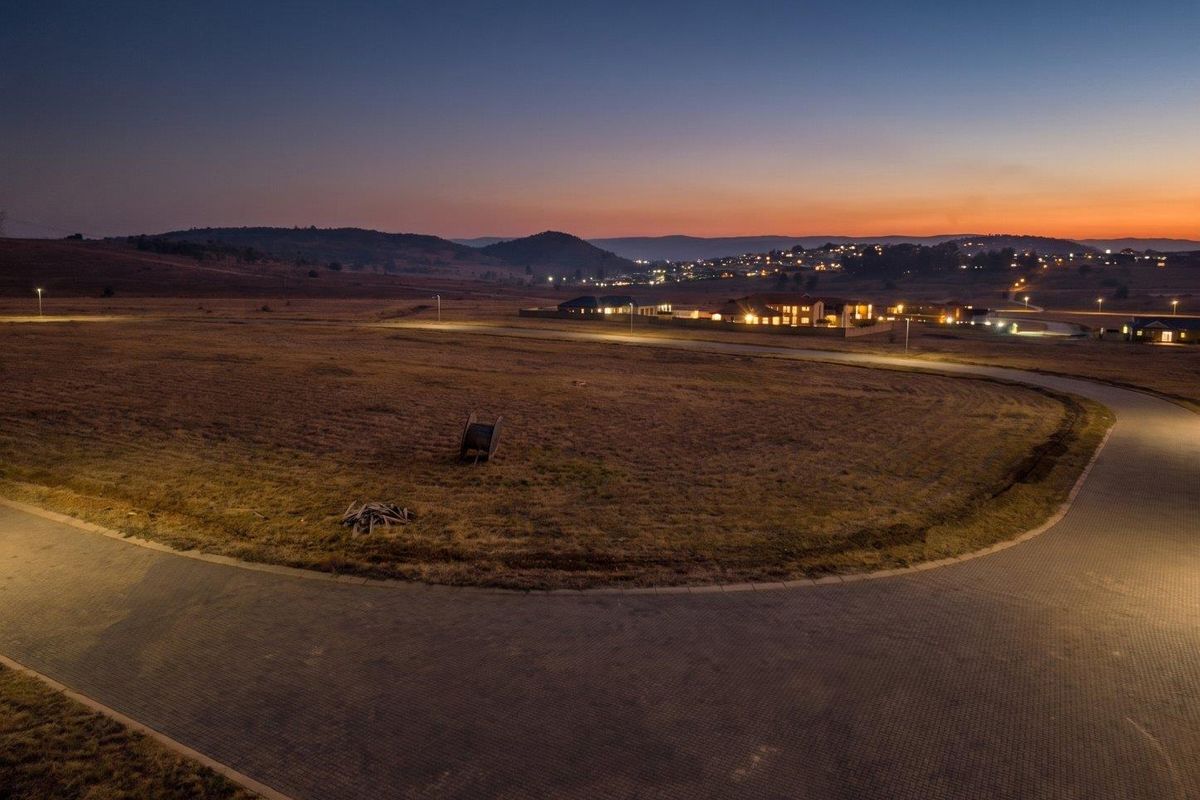 Aerial view of a vacant residential plot at dusk, featuring paved road access and established street lighting in a developing estate.