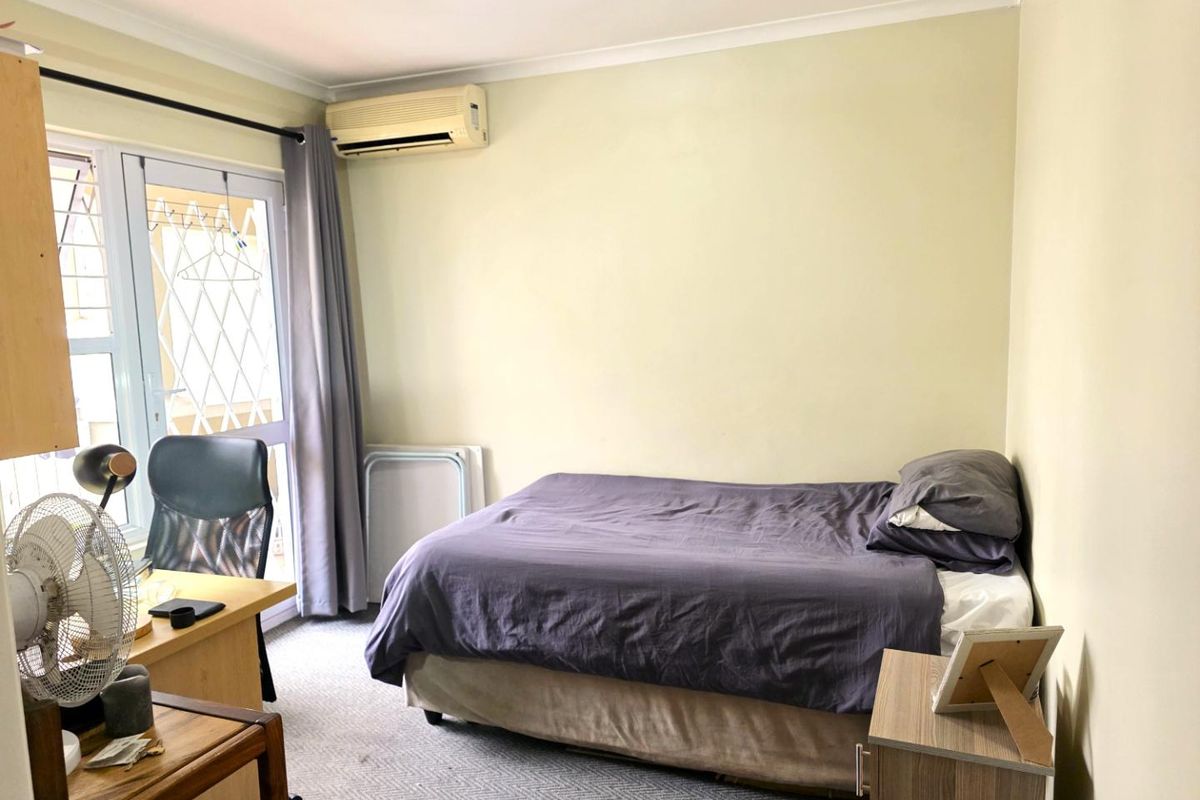 A functional bedroom featuring a wall-mounted air conditioning unit, carpeted flooring, and a glass door providing access to an outdoor area.