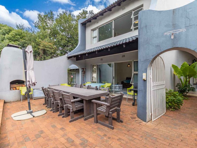 A spacious outdoor patio area featuring brick paving, a built-in braai, and direct access to the interior through sliding glass doors.