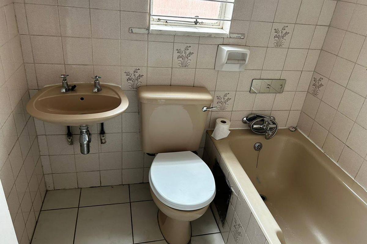 A dated bathroom featuring a beige bathtub, matching toilet, and wall-mounted basin with tiled walls and flooring.