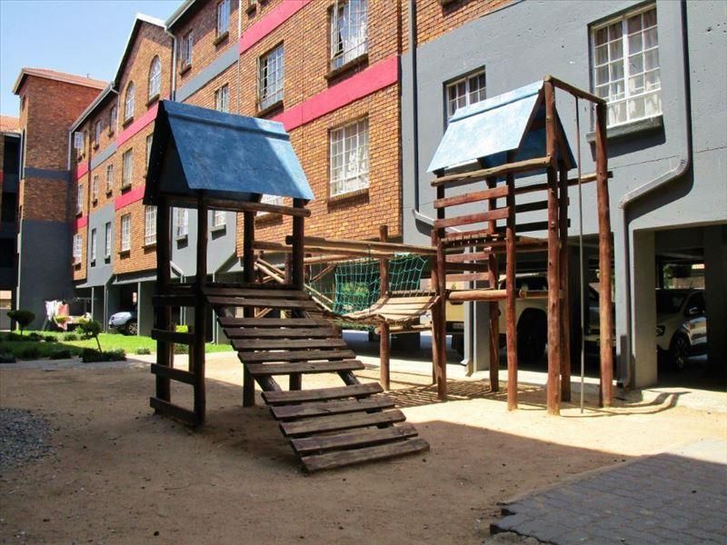 Communal outdoor area featuring a timber playground structure set against a brick apartment building with covered parking access.