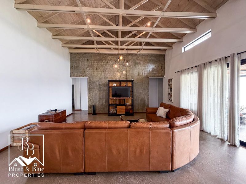 Spacious living room featuring high exposed timber trusses, polished concrete floors, and a striking feature concrete wall with integrated sliding door access.