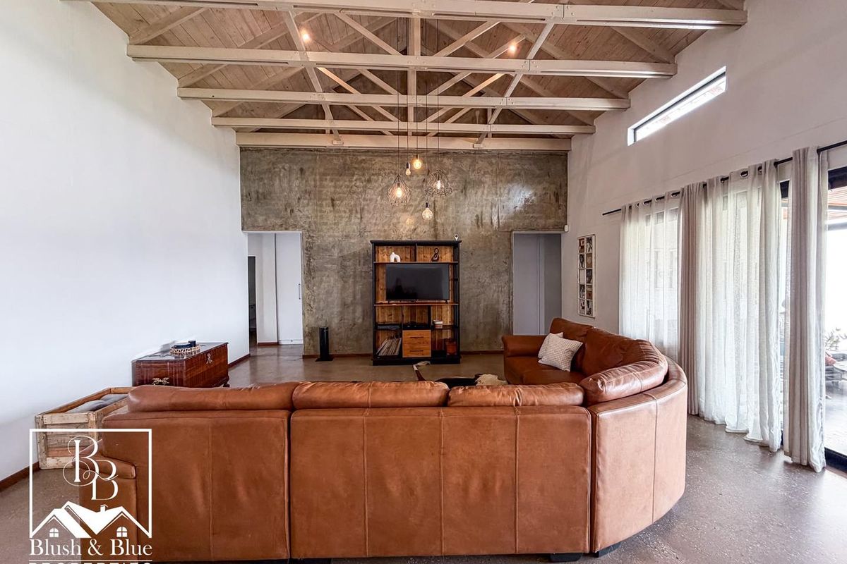 Spacious living room featuring high exposed timber trusses, polished concrete floors, and a striking feature concrete wall with integrated sliding door access.
