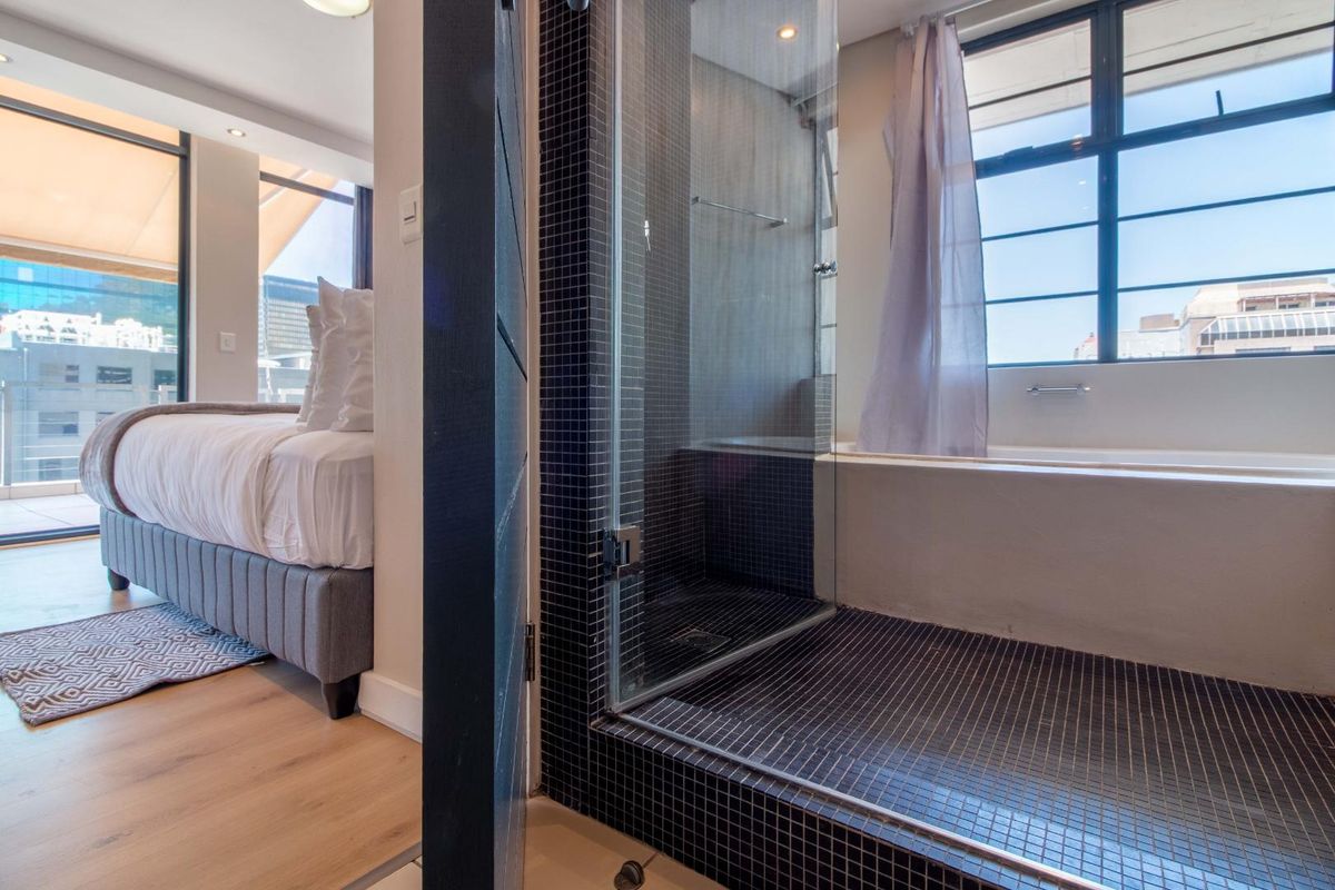 Modern bathroom featuring a glass-enclosed shower with dark mosaic tiling and a built-in bathtub adjacent to a bedroom area.
