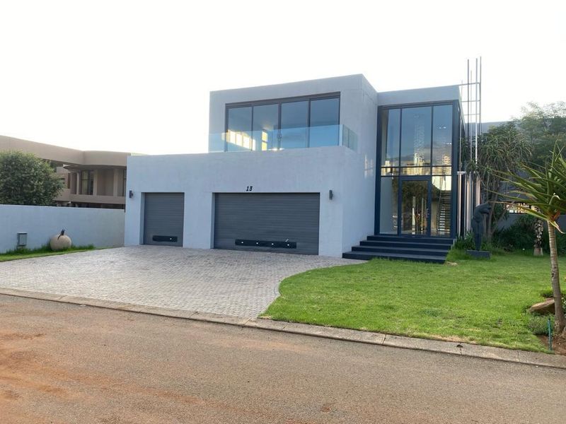 Modern double-story residence featuring a contemporary grey facade, triple garage configuration, expansive glass entrance, and a well-maintained front garden with paved driveway.