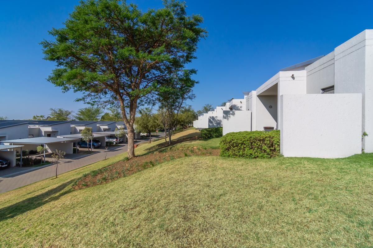 Exterior view of a modern townhouse complex featuring white rendered facades, covered parking bays, and well-maintained landscaped garden areas.