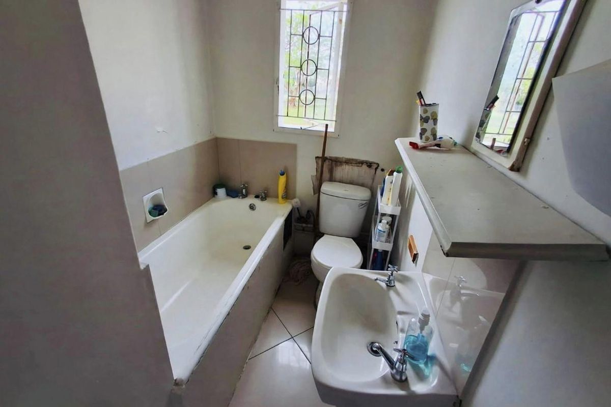 A compact bathroom featuring a bathtub, pedestal basin, and toilet, requiring cosmetic updates and repairs to the wall finishes.
