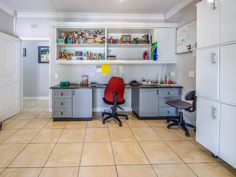 A functional home office featuring built-in desk space, extensive overhead shelving, and ample storage cabinetry with tiled flooring.