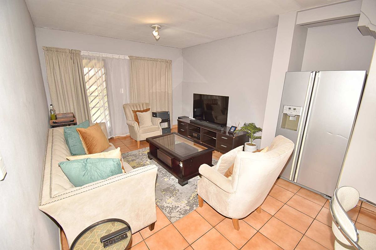 A functional living room featuring tiled flooring and a sliding glass door with security gate, providing access to the exterior.